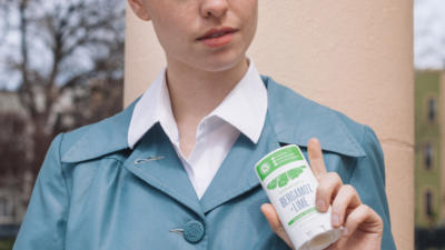 Een vrouw draagt een vintage blauwe jas met een wit overhemd met kraag en een Bergamot + Lime deodorantstick.